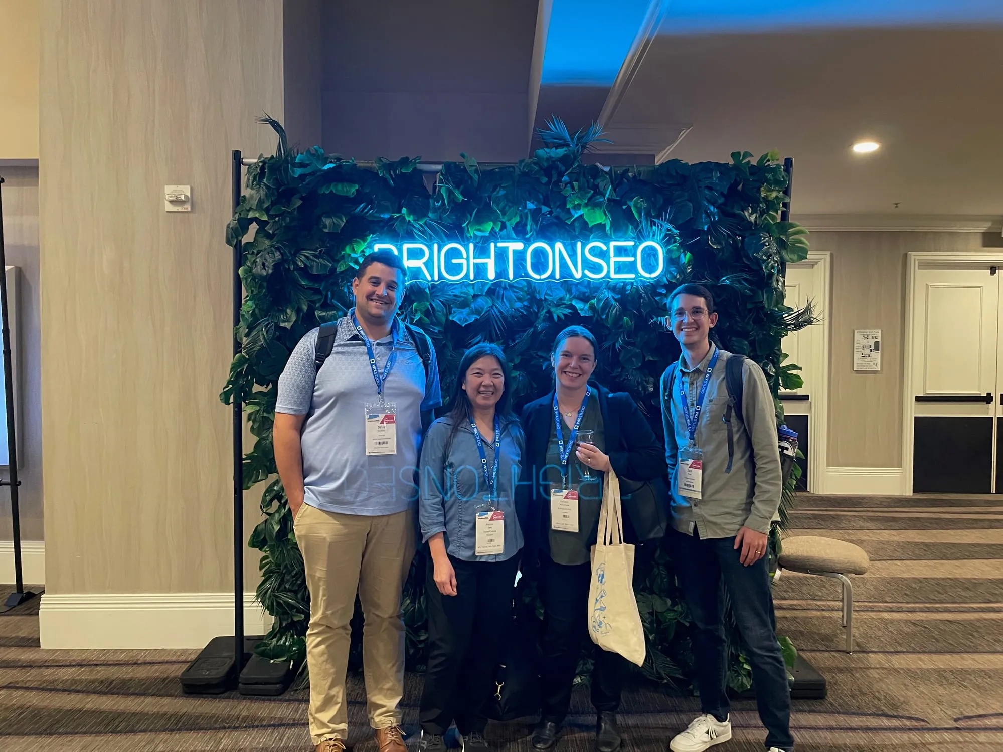 Zach with three other SEOs in front of the BrightonSEO neon sign